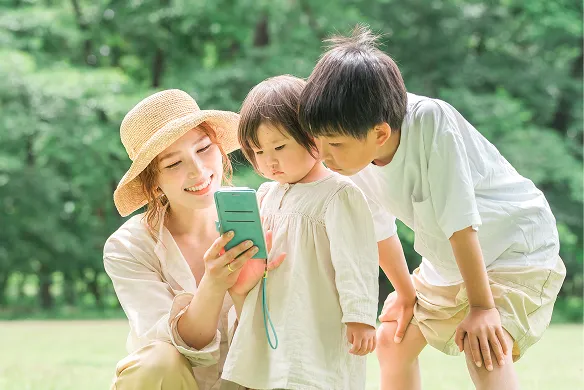 公園でスマートフォンの画面を見る母親と二人の子ども
